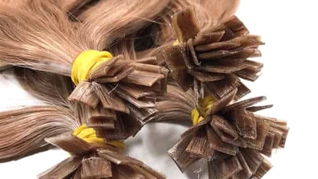 Flat tip keratin hair extension bundles with thin flat rectangular plaques fanned for wholesale salon stock QC on a white table